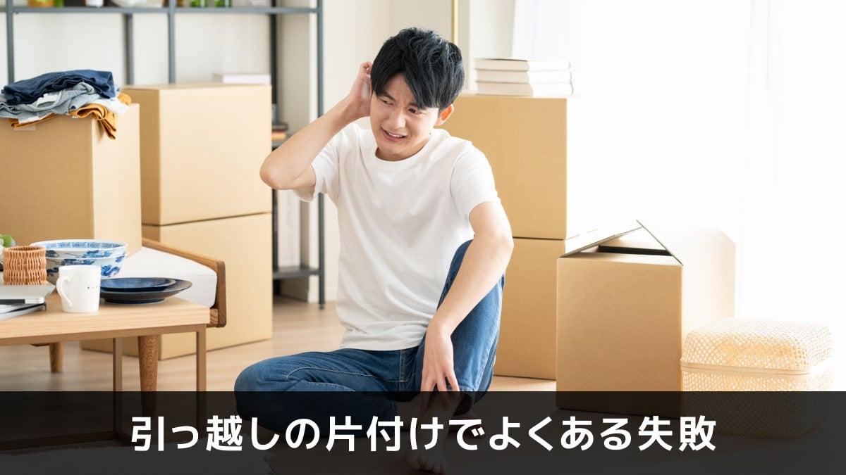写真：引っ越しの片付けでよくある失敗。ダンボールに囲まれた部屋で頭をかいている男性の写真。