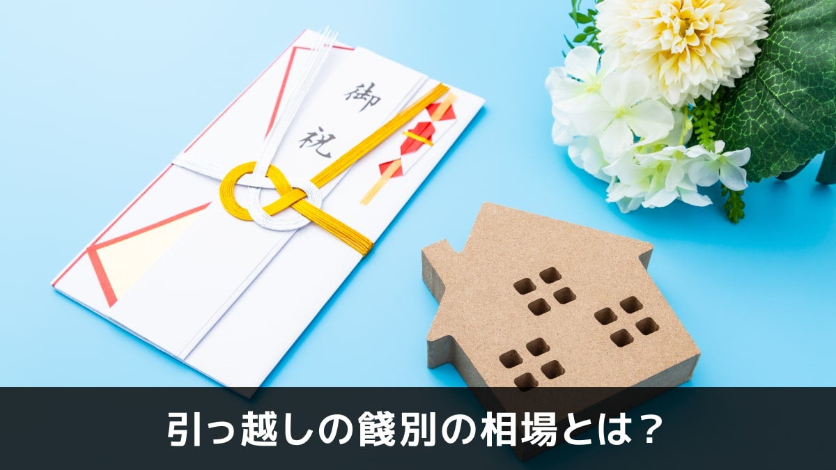 写真：引っ越しの餞別の相場とは？。御祝いの袋と家の形をした木のオブジェと花が写っている写真。