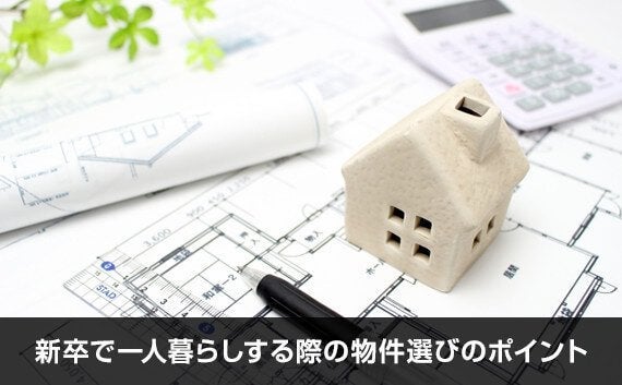 写真：新卒で一人暮らしする際の物件選びのポイント。手のひらサイズの白い家のオブジェと電卓と設計図が写っている写真。