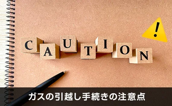 写真：ガスの引越し手続きの注意点。CAUTIONと書かれた木のオブジェとノートとペンが写っている写真。
