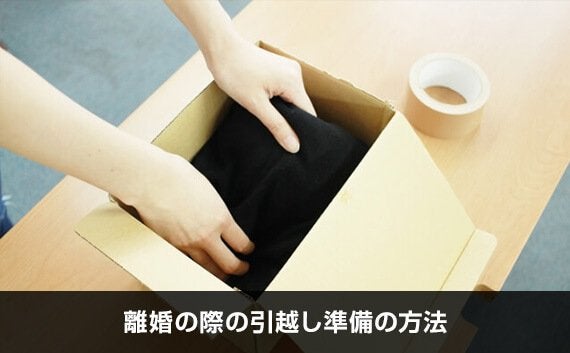 机の上で小さめのダンボールに黒い荷物を入れて荷造りしている様子